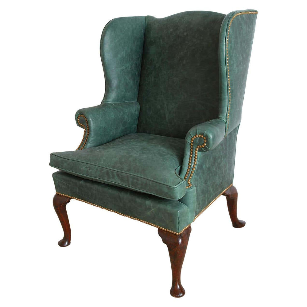 Green leather wingchair with nailhead trim and wooden legs.