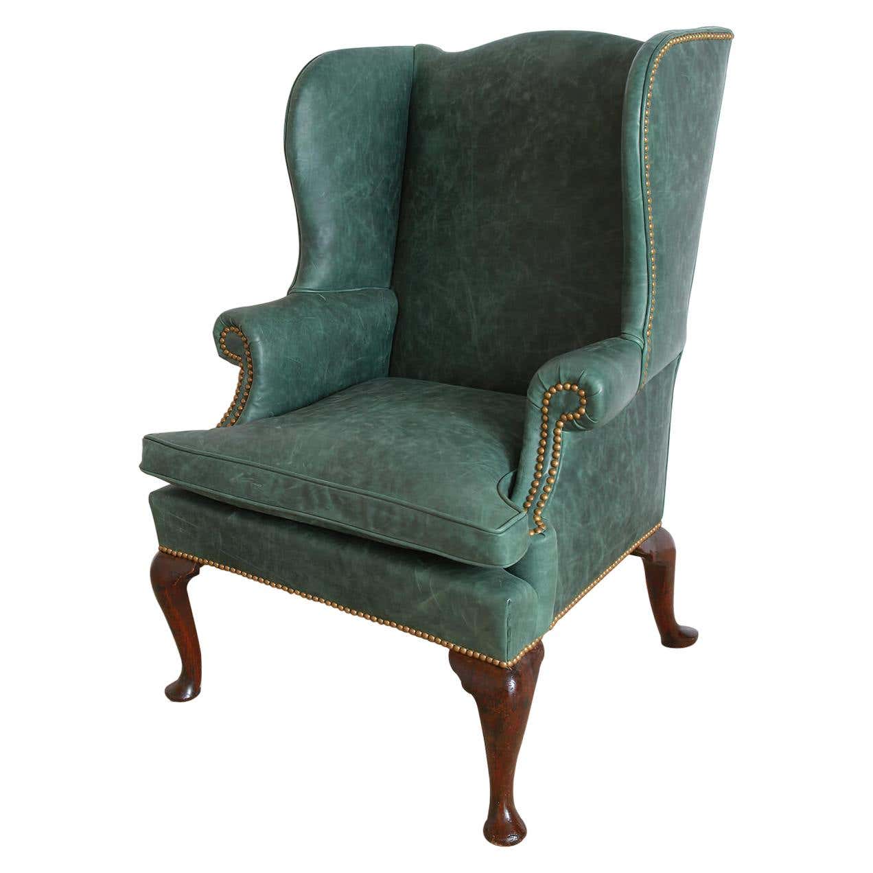 Green leather wingchair with nailhead trim and wooden legs.