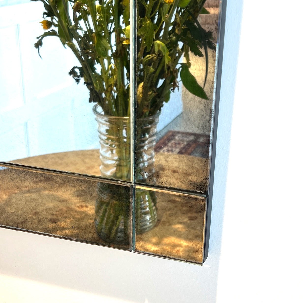 Close-up of mirror corner showing detail, reflects flowers.