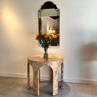 Mirror hangs above ornate table, interior setting visible.