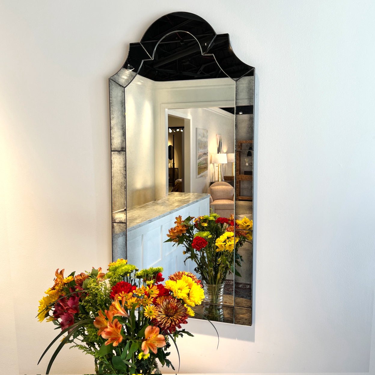 Decorative mirror on wall, reflecting colorful flowers below.