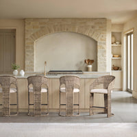 Natural rattan counter stools with cream cushions arranged at a pale kitchen island