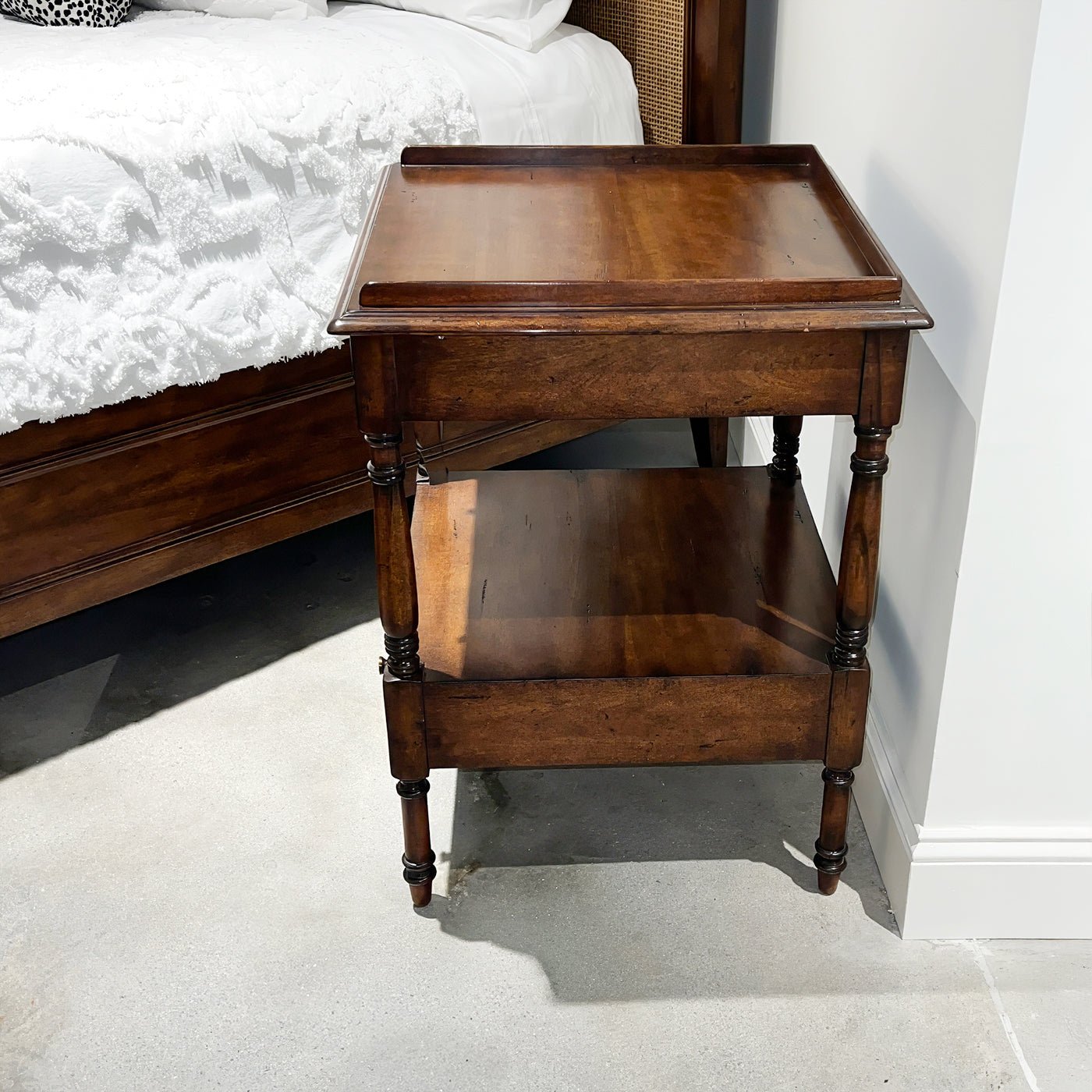 Regency style side table beside bed, side perspective.