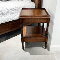 Regency style side table beside bed, side perspective.