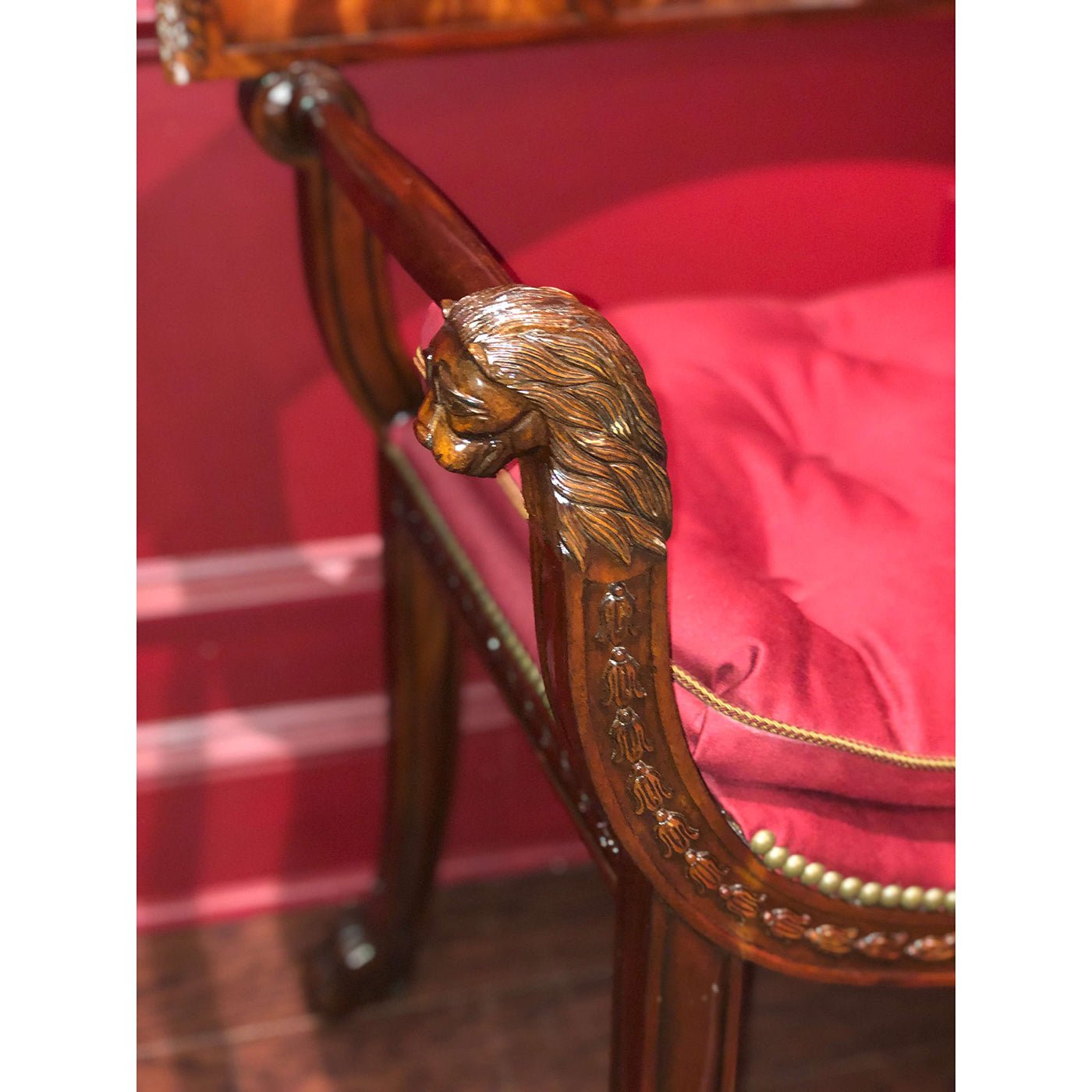 Close-up of armchair lion carving, red cushion detail.