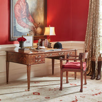 Regency style armchair, red cushion, beside wooden desk in room.