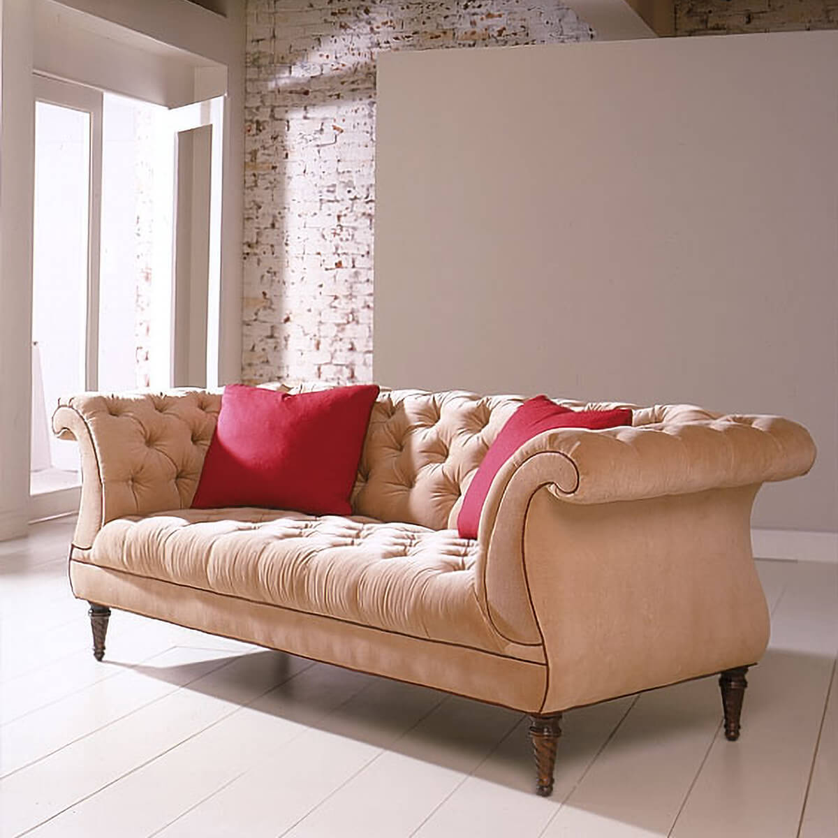 Beige tufted lyre sofa with red pillows in bright room.