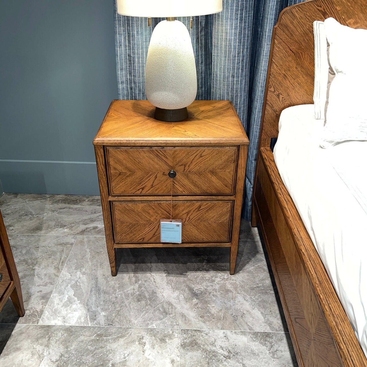 Decorated rustic light oak nightstand beside bed with lamp.