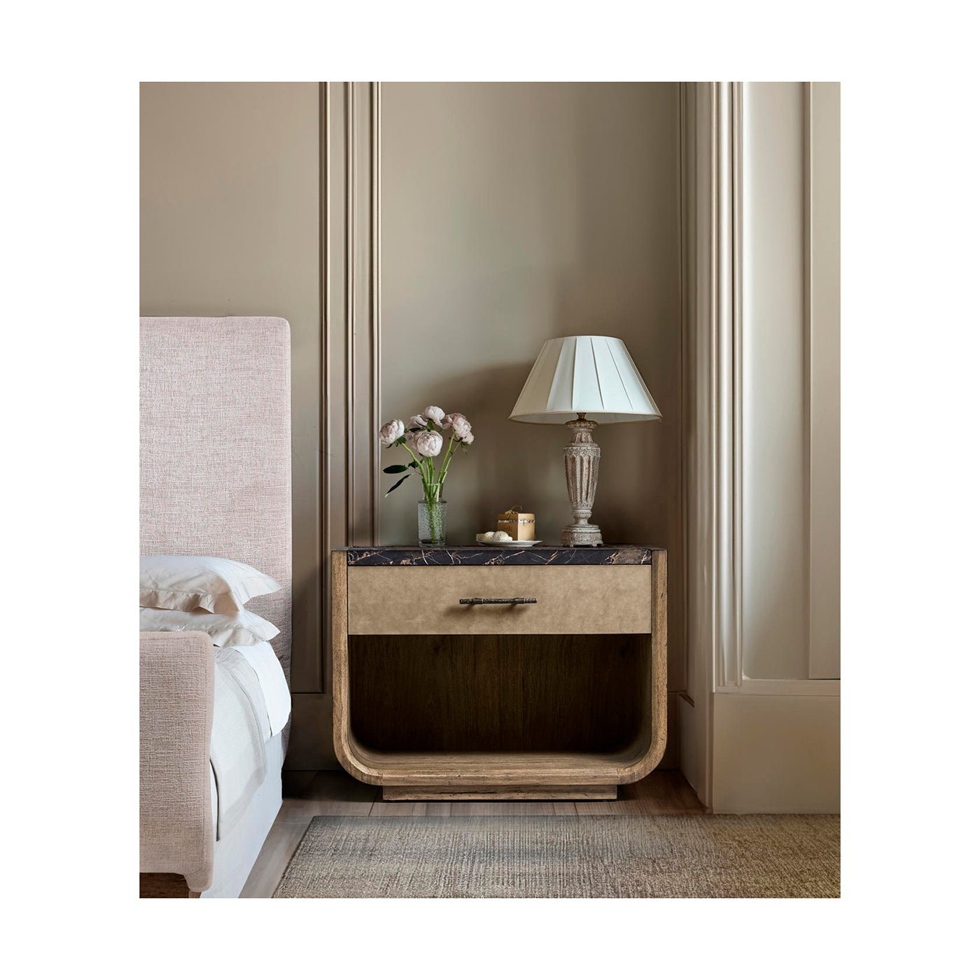 Nightstand styled in bedroom with lamp and flowers.
