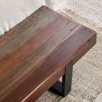 Elevated detail of the reclaimed wood bench beside a bed, showing the weathered seat and dark iron support