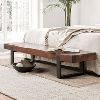 Reclaimed wood bench with dark iron supports at the foot of a bed, styled with an open book