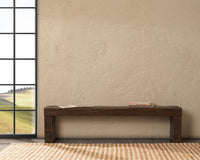 Rustic reclaimed wood bench against a textured wall beside a tall window, with books on the seat