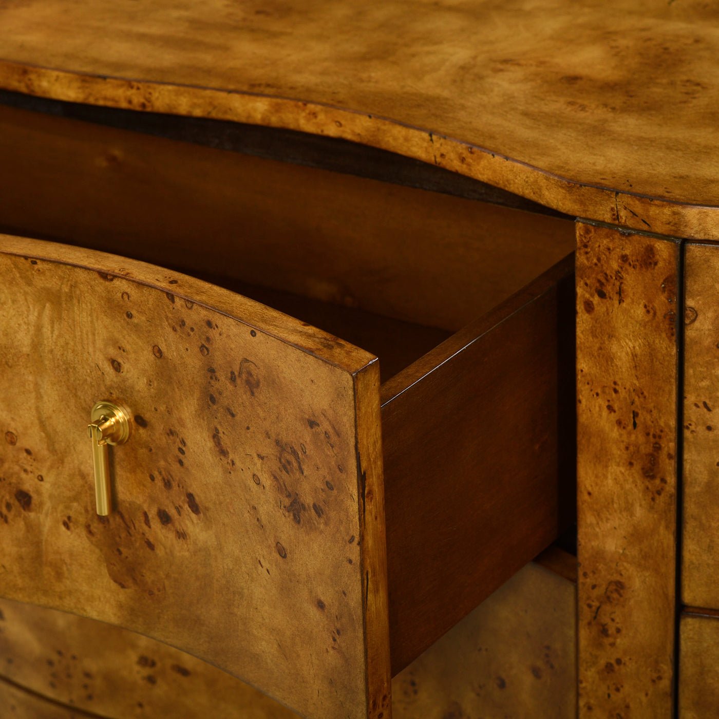 Drawer partially open on serpentine burl wood dresser.