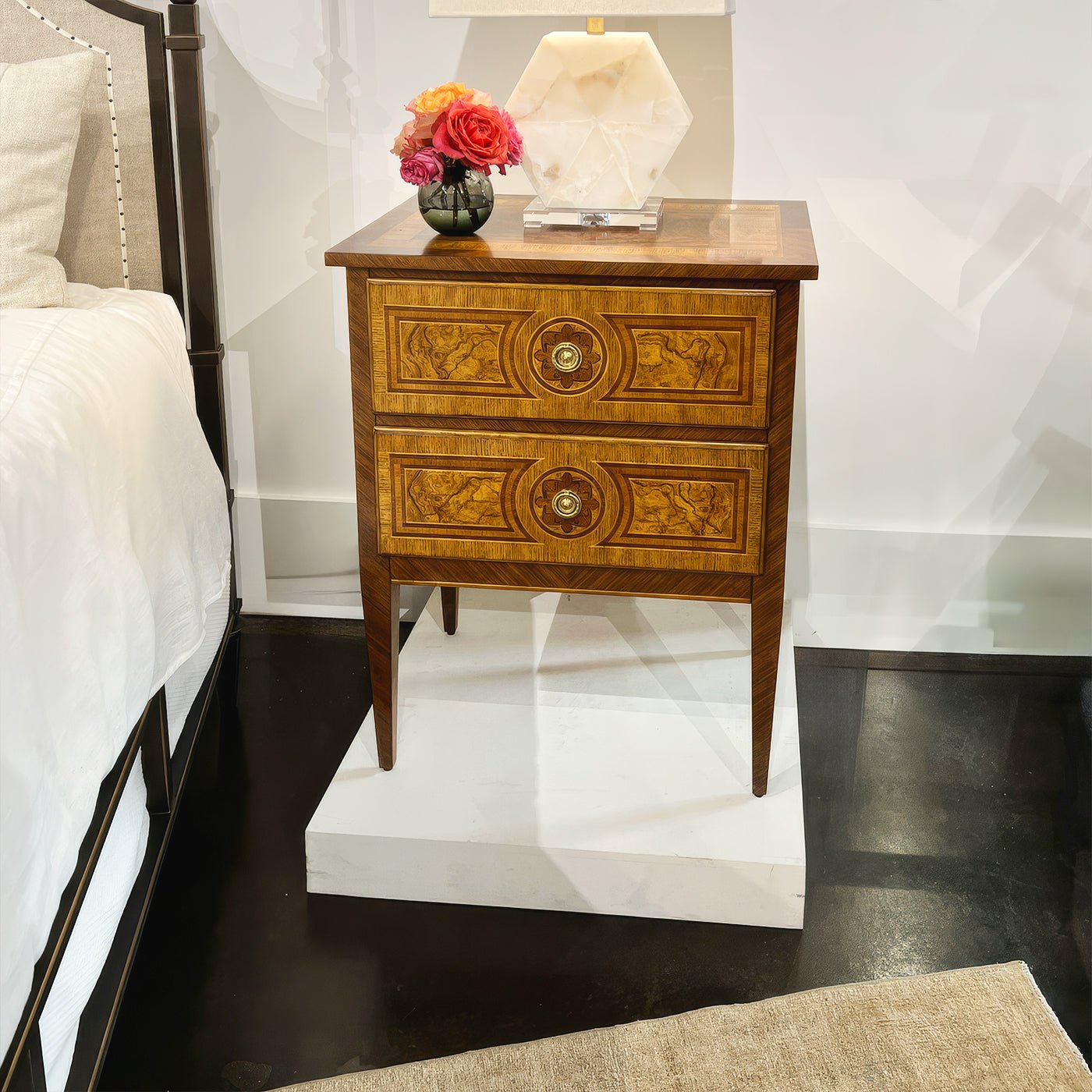 Small Louis XVI style burl nightstand beside a bed.