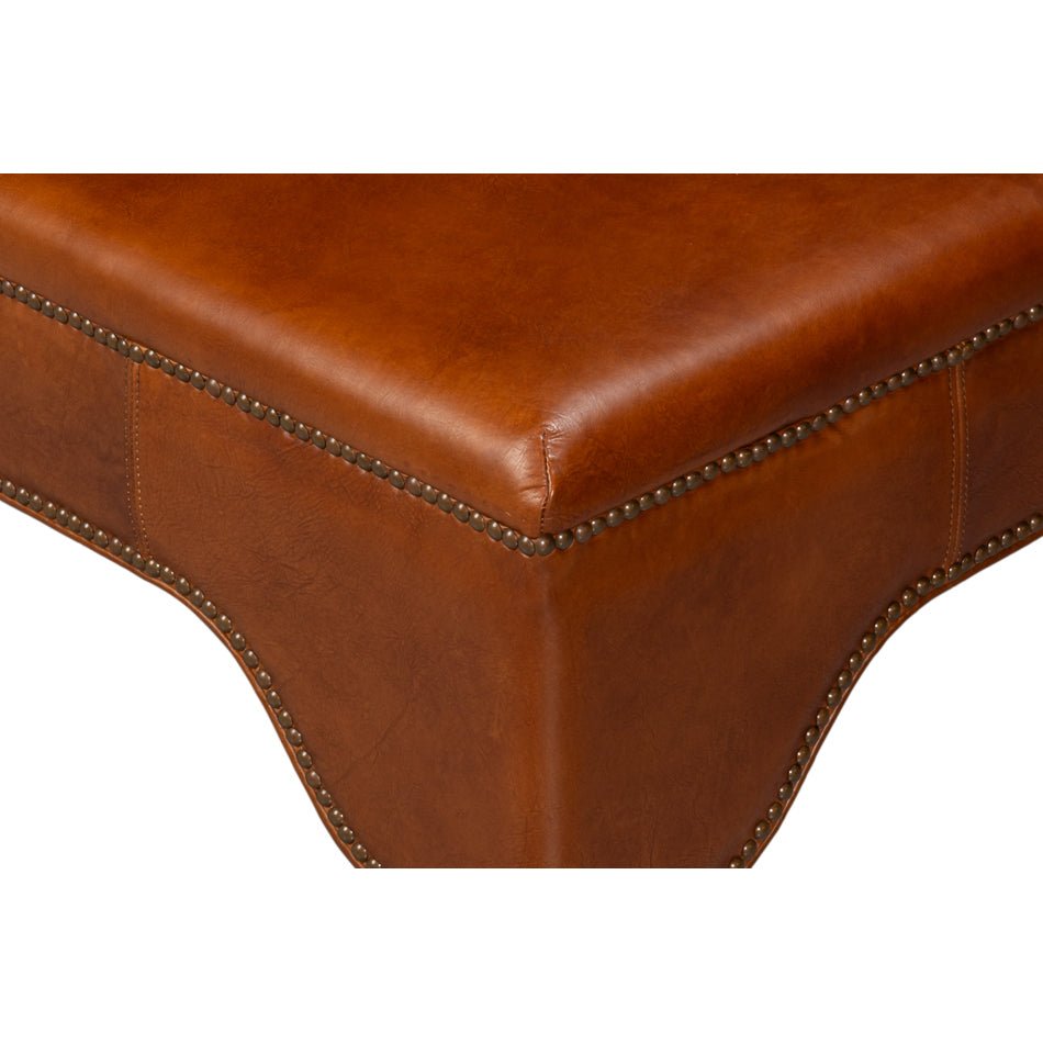 Corner detail of brown leather ottoman with nailhead trim.