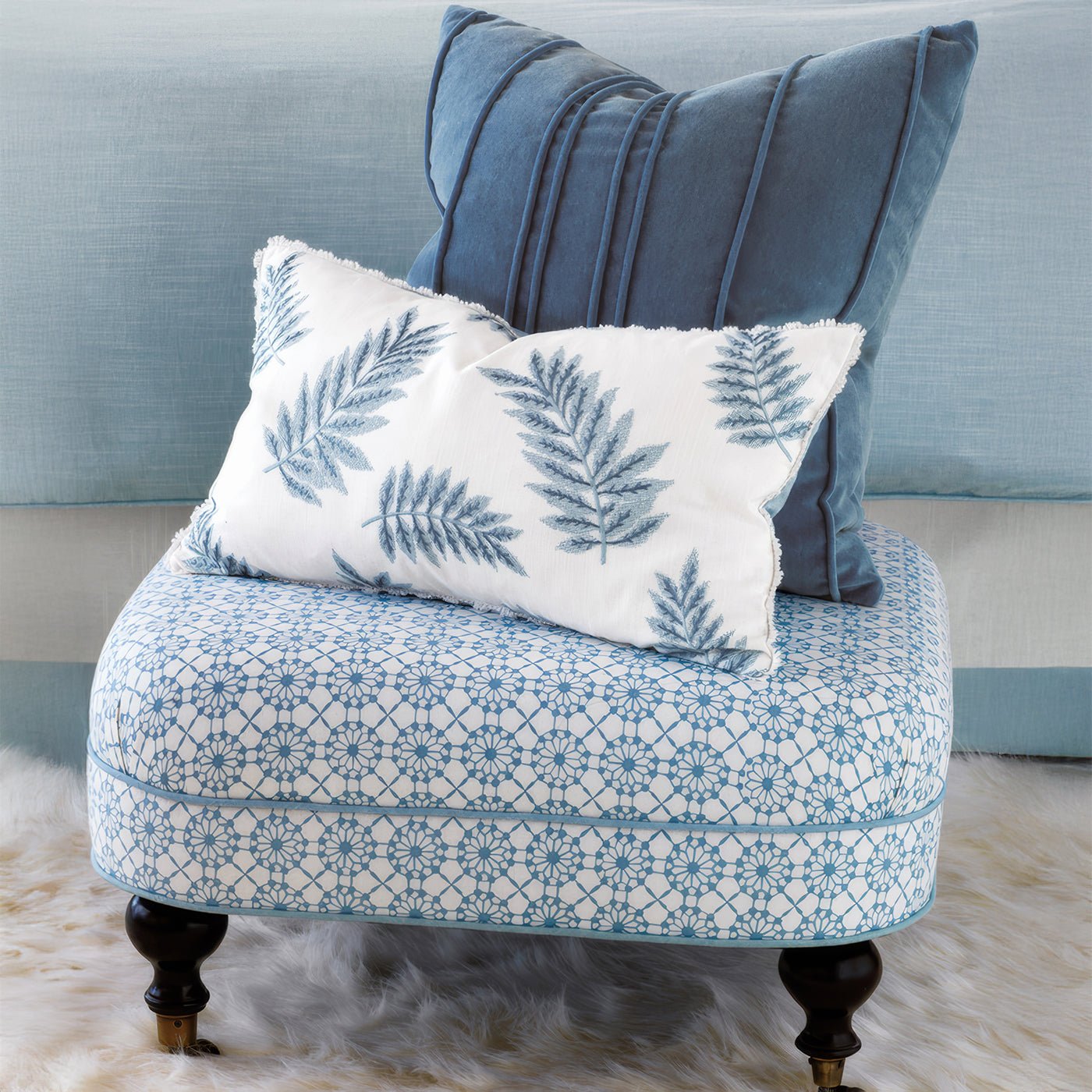 Blue-patterned ottoman with decorative pillows and fern design.