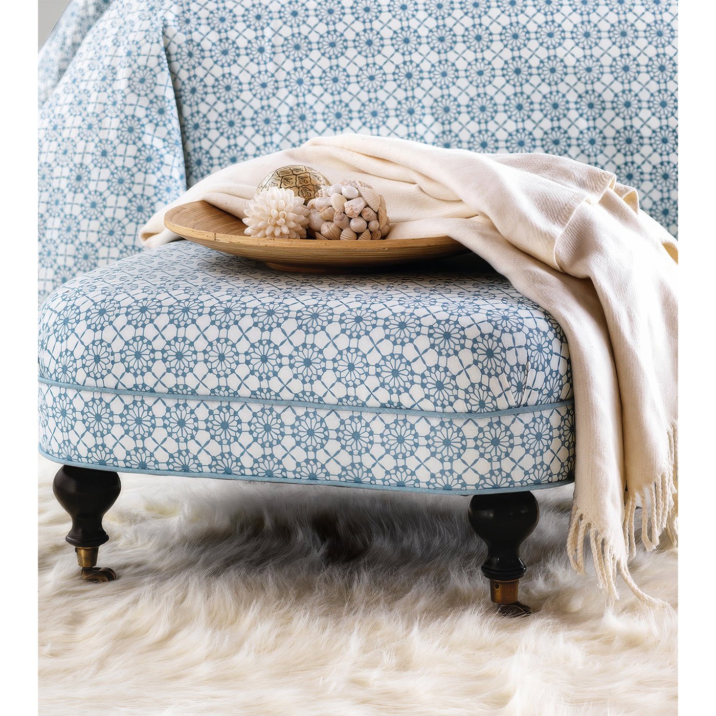 Blue-patterned ottoman with tray and beige blanket.