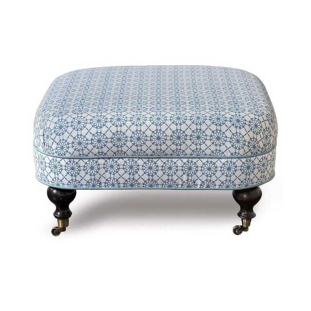 Blue-patterned ottoman with dark wooden legs on wheels.