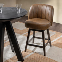 Brown leather swivel counter stool beside a round dark table on a patterned rug