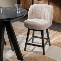 Cream fabric swivel counter stool beside a round dark table on a patterned rug