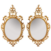 Pair of traditional Chippendale oval mirrors with intricate gold frames.