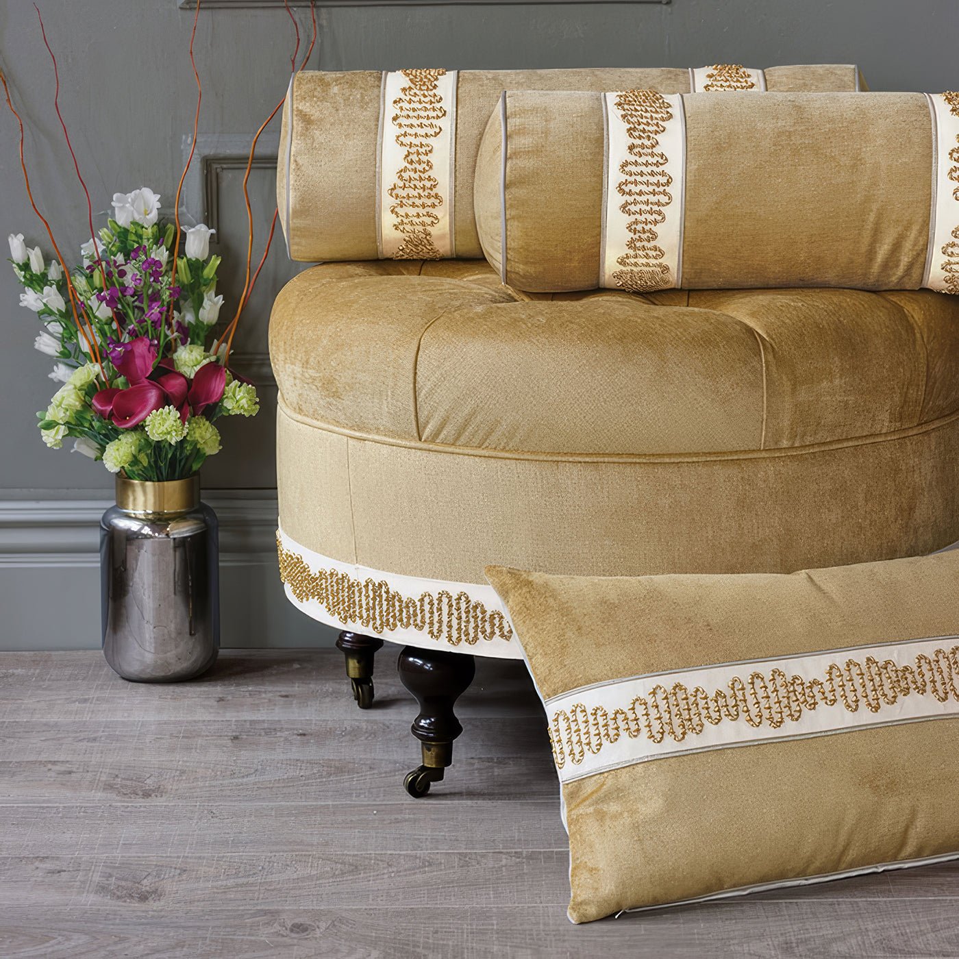 Velvet ottoman with matching cushions and floral vase.