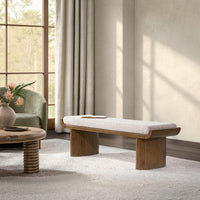 Pale upholstered bench with a curved wood frame in a sunlit living room, with an open book on the seat
