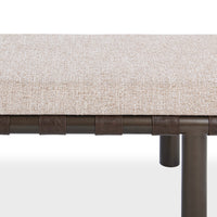 Close-up of the bench’s pale woven cushion, brown leather straps and iron leg