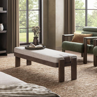 Pale upholstered bench with brown wood legs in a living room, styled with a tray beside a green armchair
