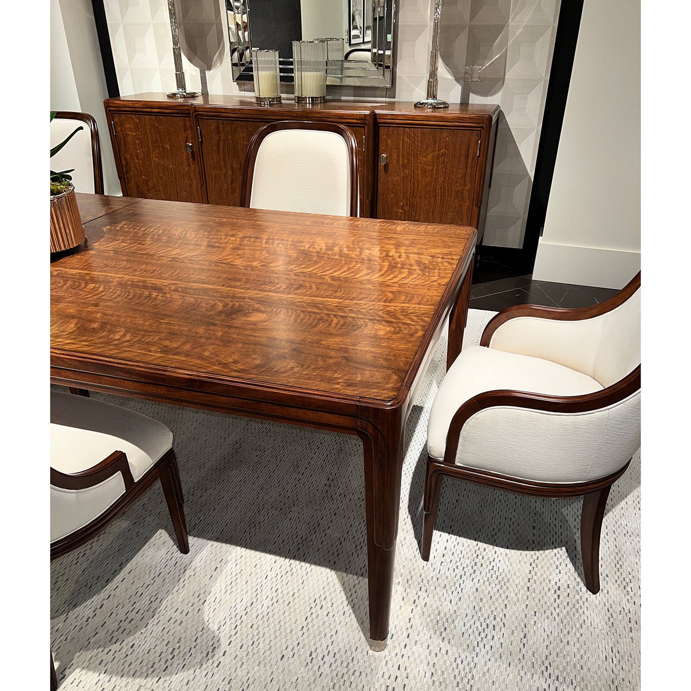 Corner view of walnut table with white chairs.