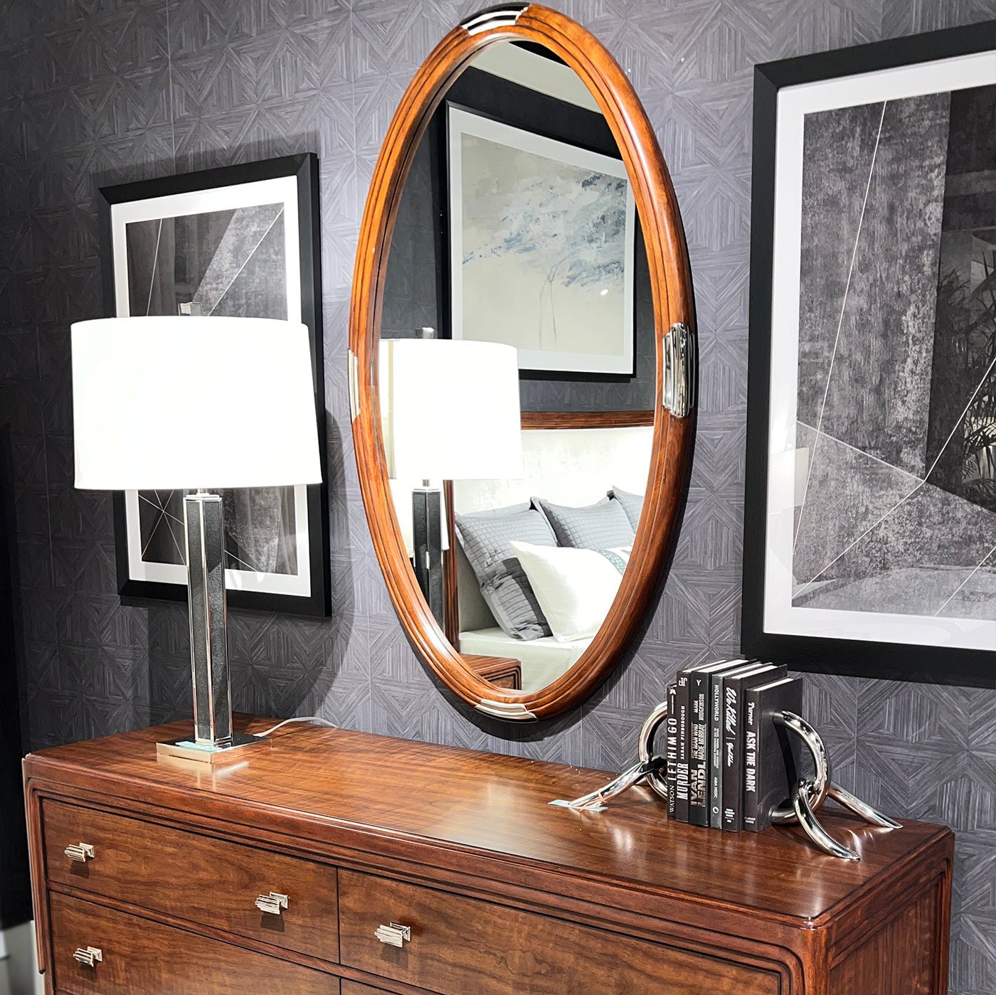 Oval Art Deco mirror above wooden dresser, elegant lighting.