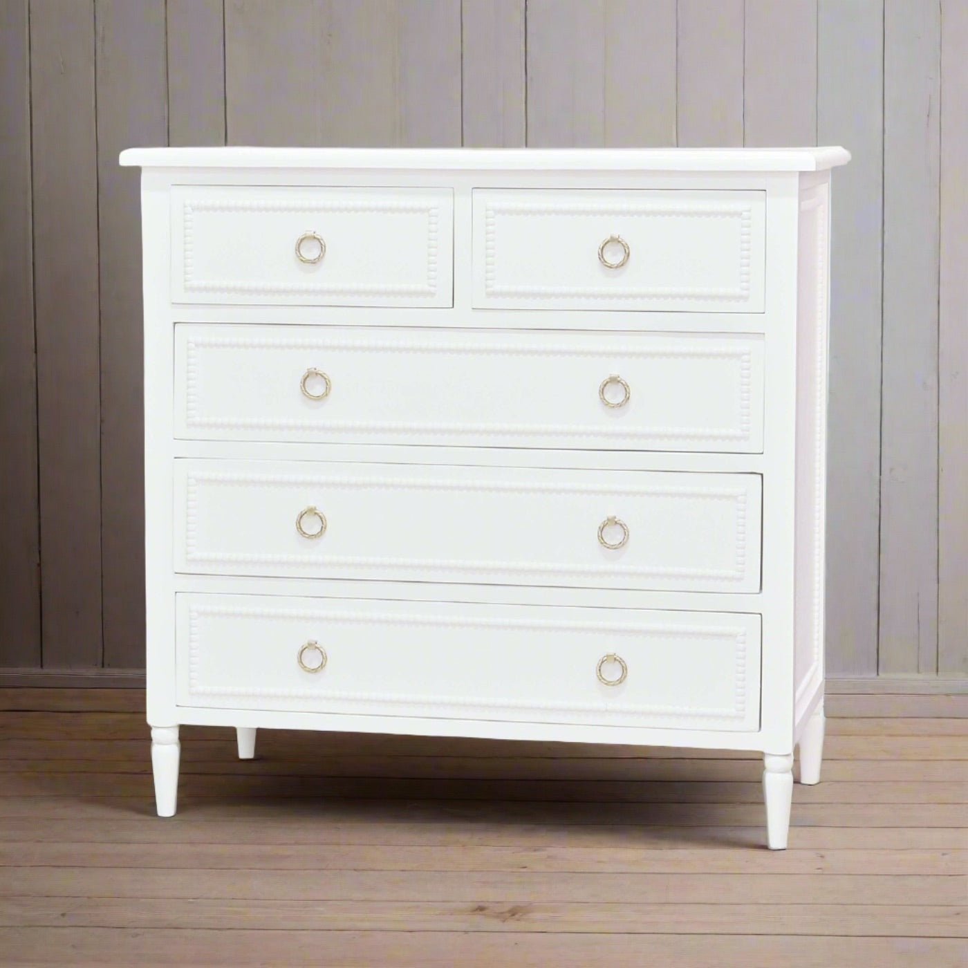White chest of drawers against wooden wall.