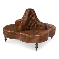 Round brown leather lobby sofa, side angle, tufted seat.